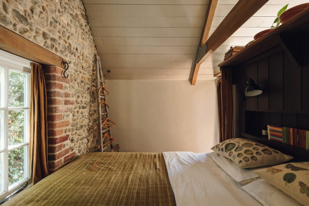 The bedroom under the eaves, with flint walls and a woven bedspread