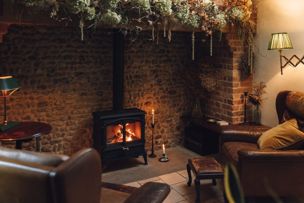 The sitting room by firelight, with leather armchairs around the woodburner