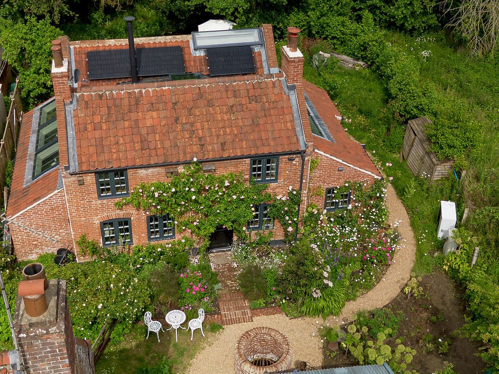 Riverbank's rose-covered front and garden from above, with the old well on the gravel path